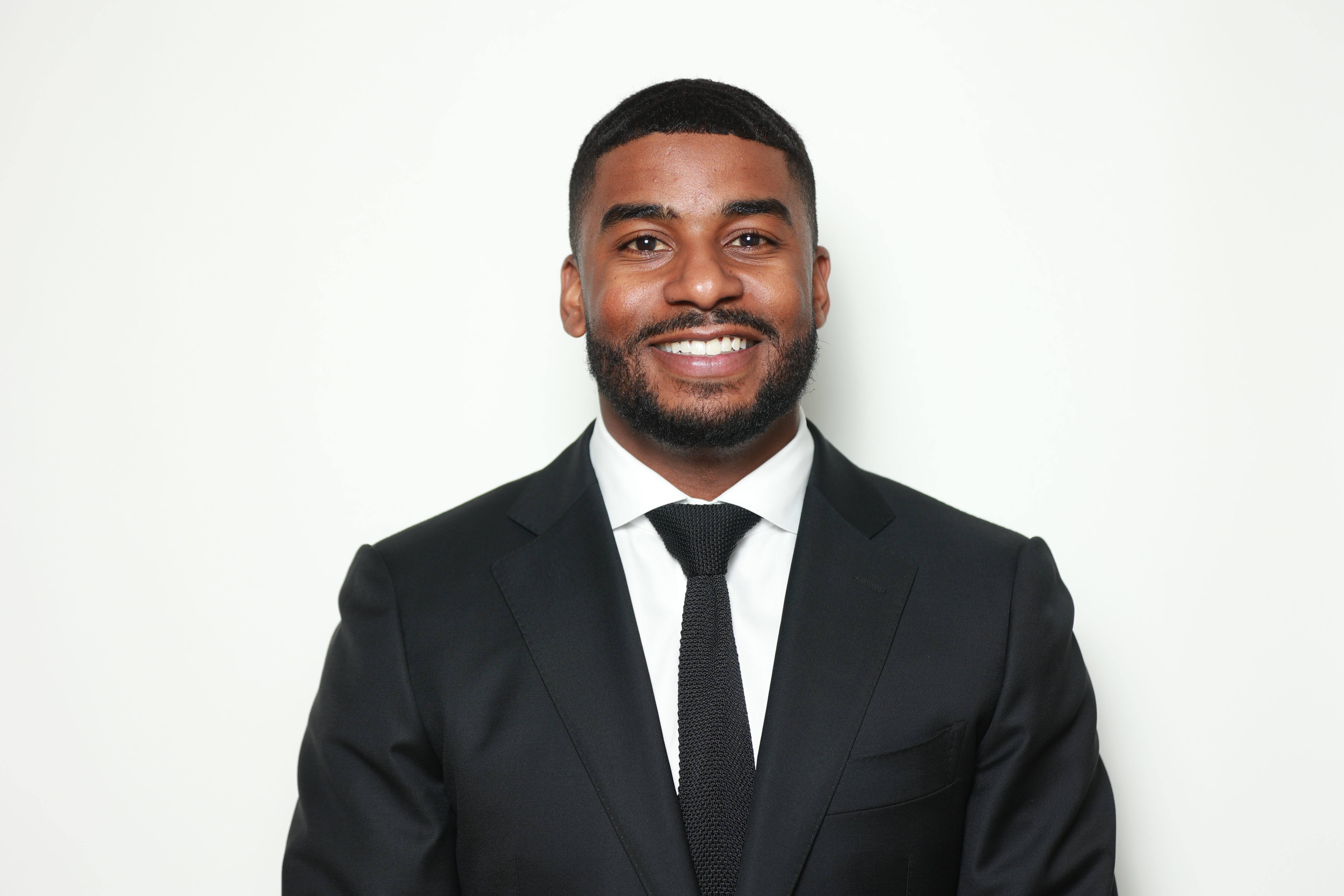 Professional headshot of a man in business attire, neutral background, confident expression